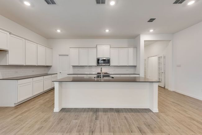 Kitchen with stainless steel microwave, dark countertops, tasteful backsplash, a center island with sink, and light wood-style floors | Image 5