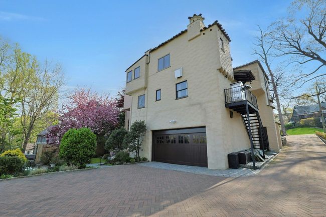 View of side of property featuring stairs, a garage, stucco siding, decorative driveway, and a chimney | Image 26