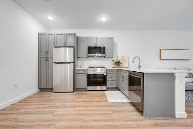 Kitchen featuring appliances with stainless steel finishes, gray cabinets, a peninsula, a sink, and light wood-style floors | Image 6