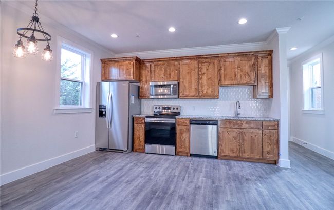 Kitchen featuring appliances with stainless steel finishes, dark hardwood / wood-style floors, sink, hanging light fixtures, and crown molding | Image 5