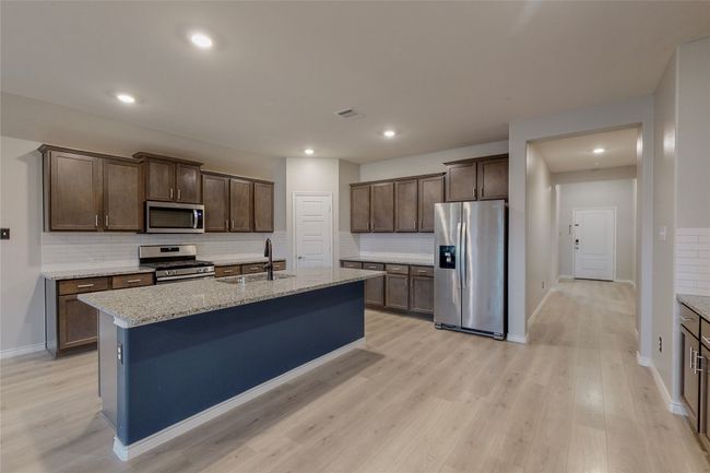 Kitchen with light wood finished floors, a sink, backsplash, baseboards, and appliances with stainless steel finishes | Image 12