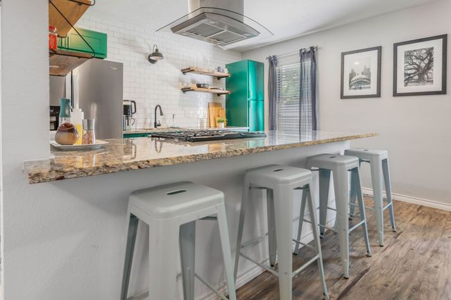 Kitchen with island exhaust hood, freestanding refrigerator, backsplash, gas stovetop, and wood finished floors | Image 12