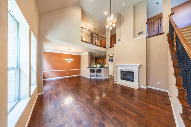 Unfurnished living room featuring a glass covered fireplace, a chandelier, dark wood-style floors, and a towering ceiling | Image 7