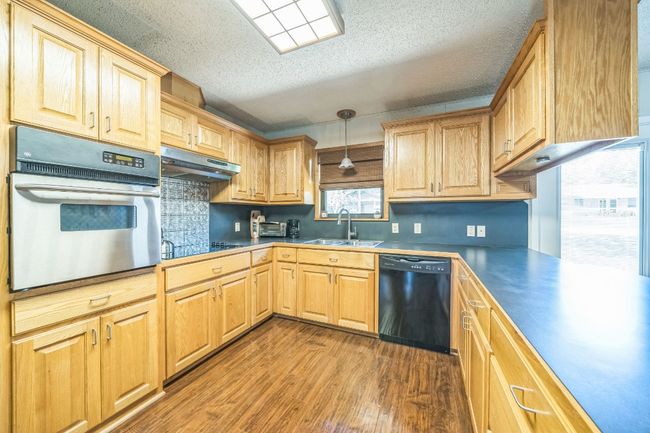 Kitchen featuring dark wood-type flooring, tasteful backsplash, black appliances, under cabinet range hood, and a sink | Image 15