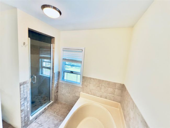 Full bathroom featuring a bath, a shower stall, tile patterned flooring, tile walls, and wainscoting | Image 10