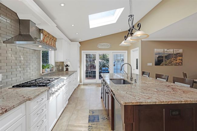 Kitchen with a sink, stainless steel appliances, wall chimney range hood, lofted ceiling with skylight, and a kitchen island with sink | Image 10