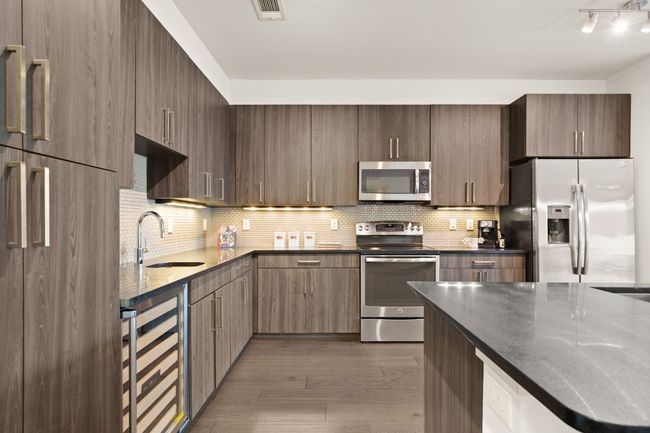 Kitchen featuring appliances with stainless steel finishes, beverage cooler, a sink, dark wood-type flooring, and decorative backsplash | Image 26