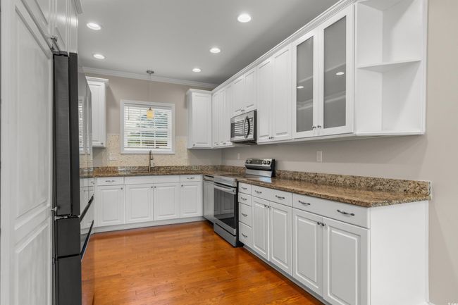 Kitchen with appliances with stainless steel finishes, ornamental molding, white cabinetry, a sink, and pendant lighting | Image 12