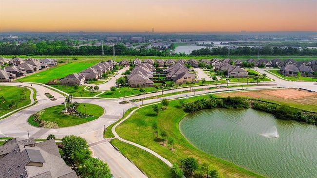 This aerial photo showcases a suburban neighborhood with modern homes, winding roads, and ample green spaces. A scenic pond with a fountain adds a serene touch, while the expansive view highlights the community's organized layout and proximity to nature. | Image 45