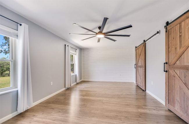Spare room with a barn door, a ceiling fan, light wood-style floors, and wooden walls | Image 16