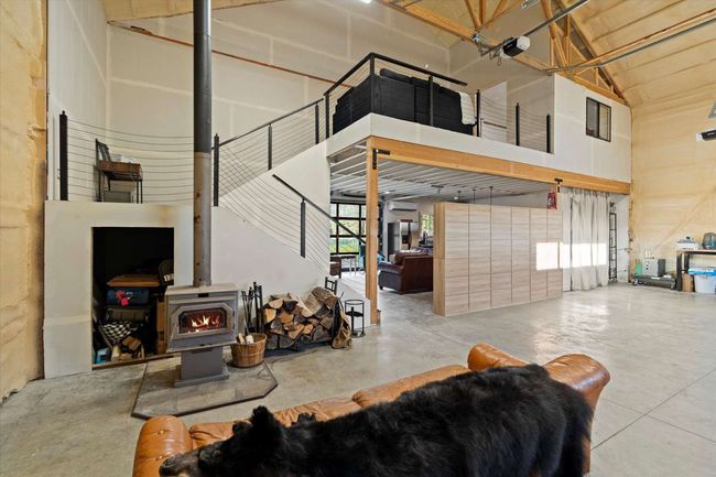 Living area with a wood stove, concrete flooring, and high vaulted ceiling | Image 12