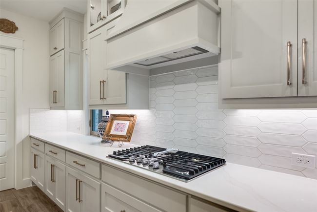 Kitchen featuring custom range hood, stainless steel gas cooktop, light countertops, decorative backsplash, and white cabinets | Image 16