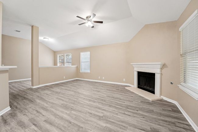 Unfurnished living room with a fireplace with raised hearth, vaulted ceiling, a ceiling fan, and light wood-type flooring | Image 7