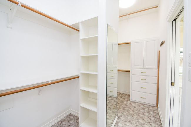Spacious walk-in closet with ample shelving, hanging rods, and built-in drawers. Features a large mirror and neutral carpet flooring, offering a bright and organized storage space. | Image 31