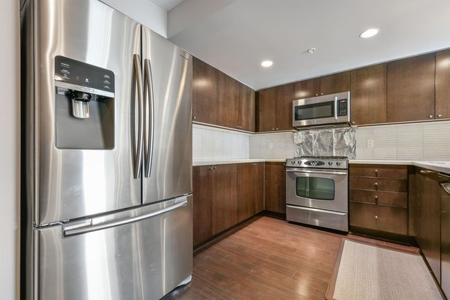 Kitchen with appliances with stainless steel finishes, light countertops, dark wood-style floors, backsplash, and dark brown cabinets | Image 12