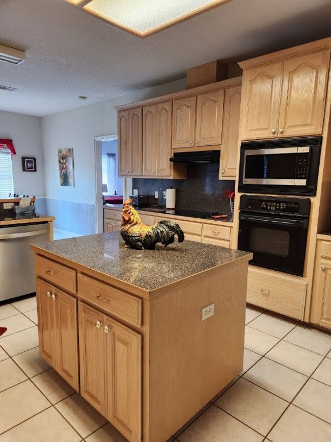 Kitchen with black appliances, light brown cabinetry, under cabinet range hood, a kitchen island, and light tile patterned floors | Image 24