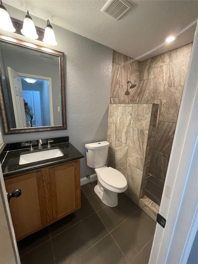 Bathroom with a textured ceiling, vanity, tiled shower, tile patterned flooring, and toilet | Image 8