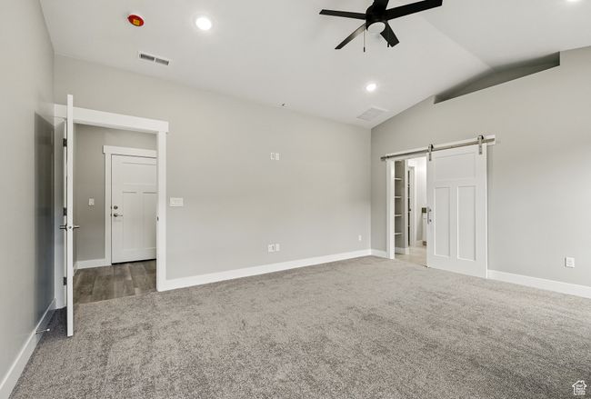 Unfurnished bedroom with a barn door, carpet flooring, vaulted ceiling, baseboards, and ceiling fan | Image 26