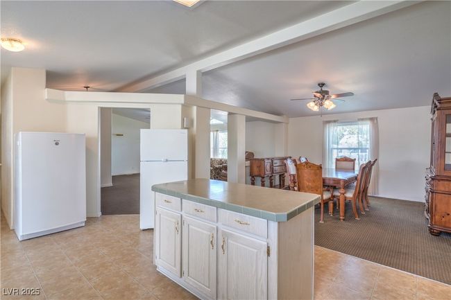 Kitchen with freestanding refrigerator, tile counters, light colored carpet, a ceiling fan, and a center island | Image 16
