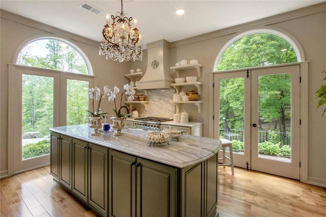 Kitchen with light stone countertops, custom range hood, light hardwood / wood-style floors, and a kitchen island with sink | Image 15