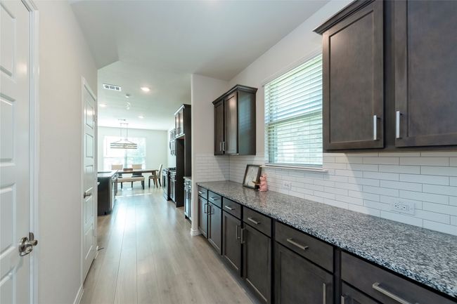 Kitchen with backsplash, light stone countertops, light wood-style floors, dark brown cabinetry, and recessed lighting | Image 12