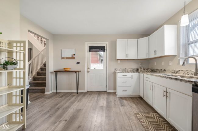 kitchen with light stone countertops, light wood-style flooring, white cabinets, a sink, and baseboards | Image 9