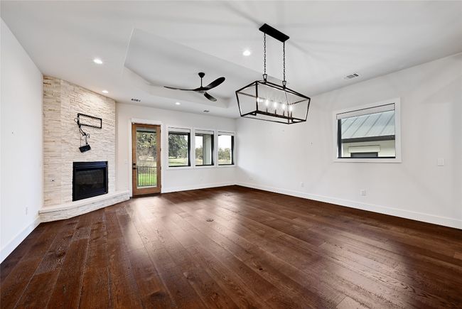 Unfurnished living room with baseboards, a stone fireplace, hardwood / wood-style floors, and ceiling fan with notable chandelier | Image 5