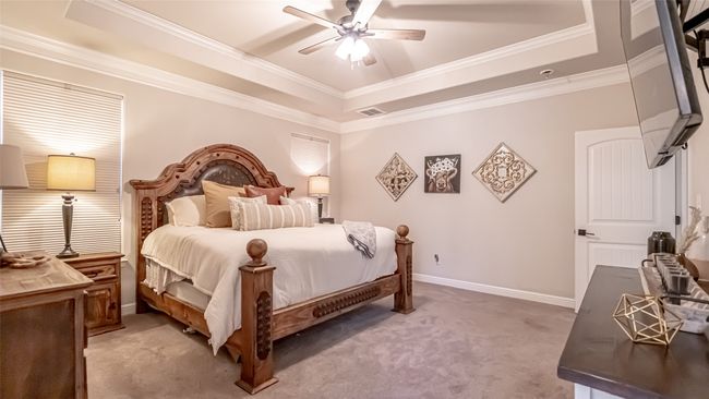 Primary bedroom with a tray ceiling, light carpet, ornamental molding, baseboards, and a ceiling fan | Image 11