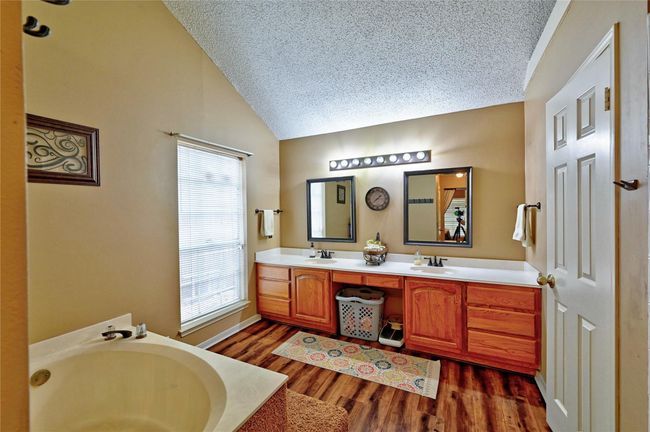 Luxurious ensuite bath featuring dual sinks, a spacious vanity, and a relaxing tub, all complemented by warm wood accents and ample natural light. | Image 21