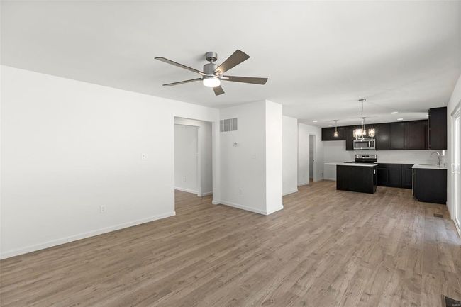 Unfurnished living room with ceiling fan with notable chandelier, light wood-type flooring, and sink | Image 18
