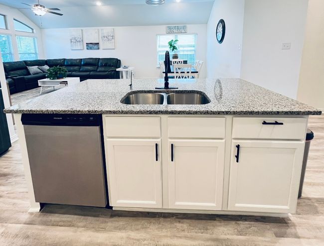 Kitchen featuring stainless steel dishwasher, a sink, light wood-style floors, a ceiling fan, and light stone countertops | Image 12
