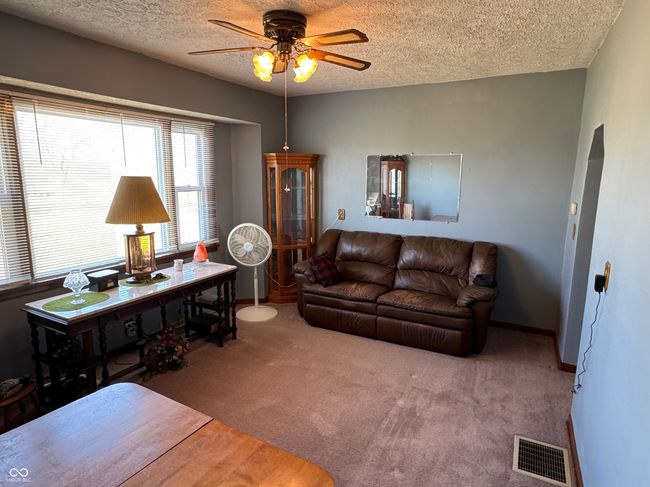 living area featuring baseboards, a textured ceiling, carpet floors, visible vents, and a ceiling fan | Image 22