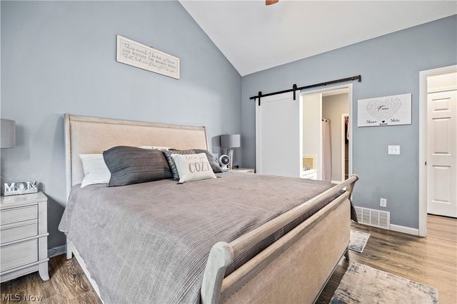 Bedroom featuring lofted ceiling, wood-type flooring, a barn door, ensuite bathroom, and ceiling fan | Image 19