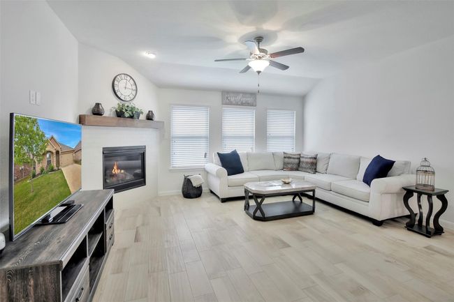 Living room featuring ceiling fan, a glass covered fireplace, baseboards, and wood finished floors | Image 11