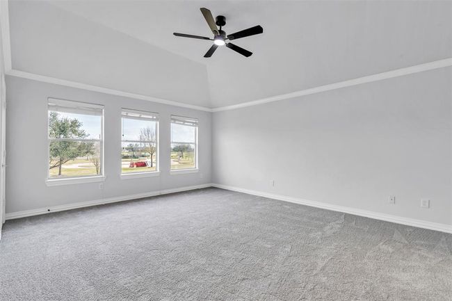 Spacious, bright room with large windows offering plenty of natural light and scenic views. Features a vaulted ceiling with a modern ceiling fan and neutral carpeting, creating a cozy and inviting atmosphere. | Image 26