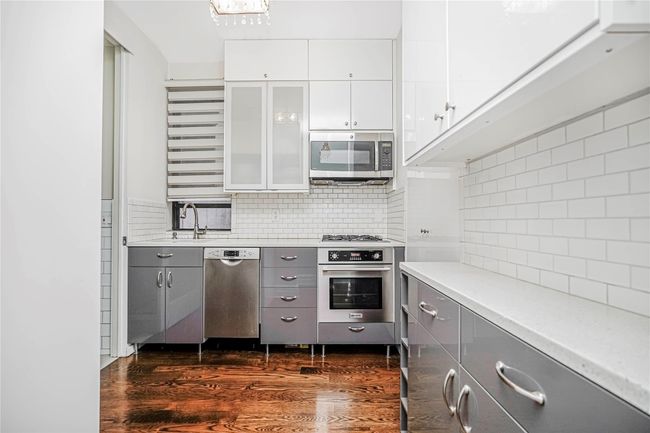 Kitchen featuring stainless steel appliances, gray cabinetry, decorative backsplash, light countertops, and glass insert cabinets | Image 11