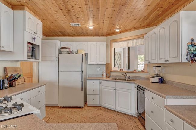 Kitchen with freestanding refrigerator, wood ceiling, a sink, dishwashing machine, and white cabinets | Image 30