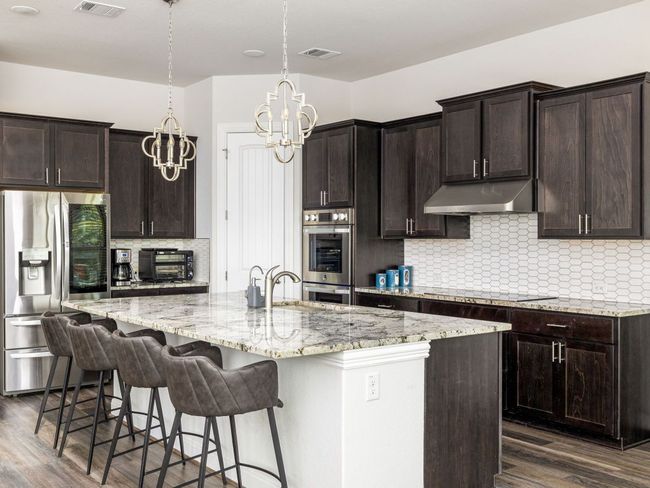 Kitchen featuring a notable chandelier, a sink, under cabinet range hood, stainless steel appliances, and dark wood-type flooring | Image 6