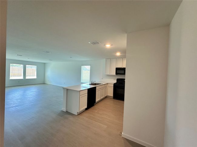 Kitchen with black appliances, a sink, baseboards, a peninsula, and white cabinets | Image 4