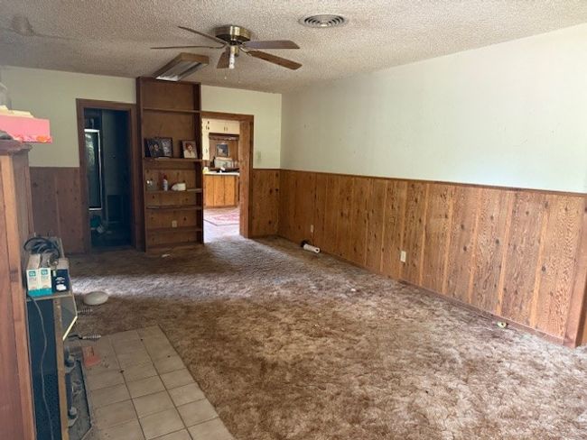 Carpeted empty room with a wainscoted wall, wooden walls, ceiling fan, and a textured ceiling | Image 8