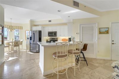 Kitchen with white cabinetry, a kitchen bar, an inviting chandelier, stainless steel appliances, and decorative light fixtures | Image 3