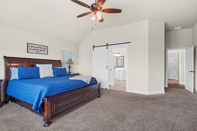 Carpeted bedroom with a barn door, vaulted ceiling, connected bathroom, and ceiling fan | Image 20