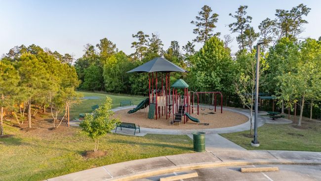 This photo shows a well-maintained playground with slides, swings, and climbing structures, set in a lush green park surrounded by trees. Ideal for families, it offers a relaxing community space with benches and a picnic area. | Image 44