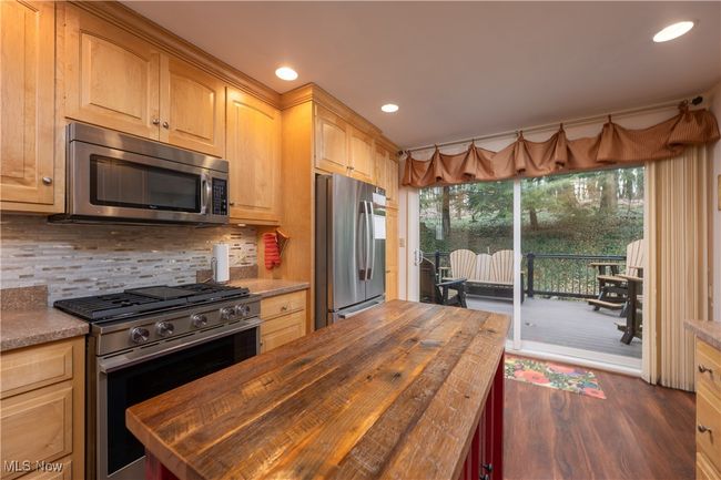 Kitchen featuring butcher block countertops, decorative backsplash, stainless steel appliances, dark wood-type flooring, and light brown cabinets | Image 22