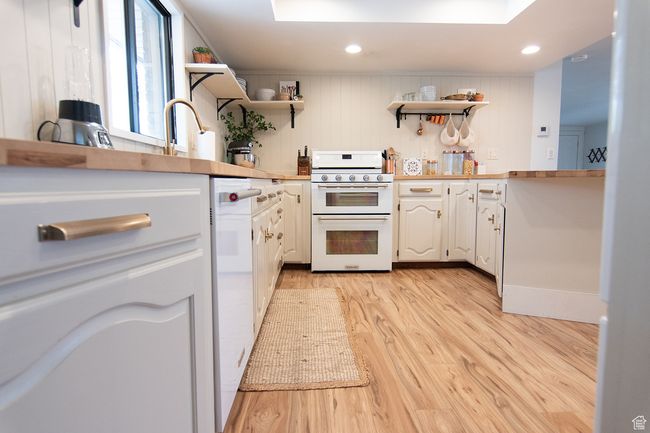 Kitchen featuring range with two ovens, open shelves, light wood finished floors, white cabinets, and a sink | Image 7