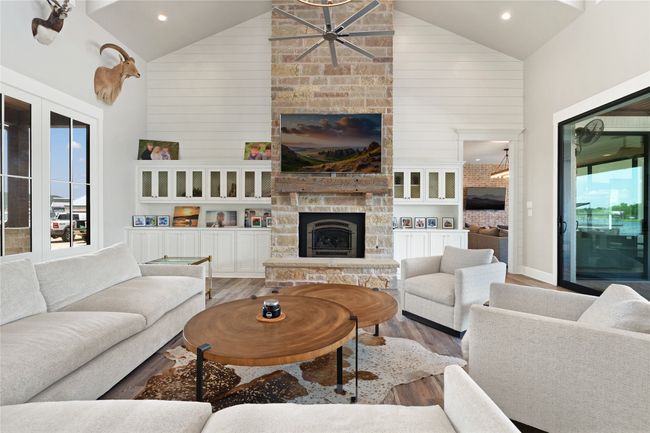 Living area with a stone fireplace, high vaulted ceiling, wood finished floors, a ceiling fan, and recessed lighting | Image 8