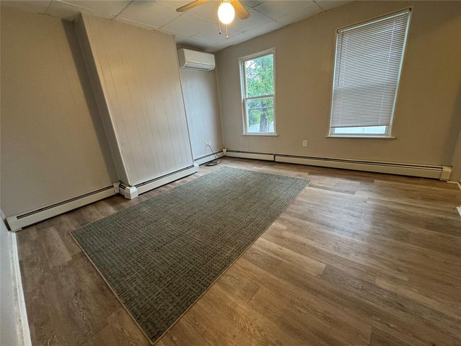 Empty room with a wall unit AC, a baseboard radiator, a ceiling fan, and wood finished floors | Image 4