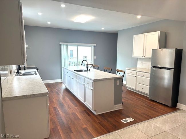 Kitchen with stainless steel fridge, tasteful backsplash, sink, a kitchen island with sink, and white cabinetry | Image 5