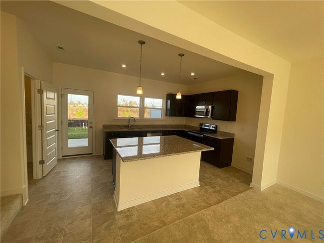 Kitchen with light stone countertops, stainless steel appliances, decorative light fixtures, a center island, and recessed lighting | Image 5