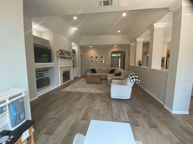 Living room featuring vaulted ceiling, a glass covered fireplace, wood finished floors, built in shelves, and baseboards | Image 11